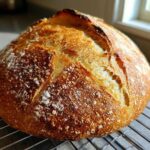 Close-up of a freshly baked, round loaf of Italian bread with a deeply browned, crackled crust cooling on a wire rack.