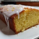 Close-up of a moist slice of lemon pound cake topped with thick white icing and lemon zest.