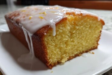 Close-up of a moist slice of lemon pound cake topped with thick white icing and lemon zest.
