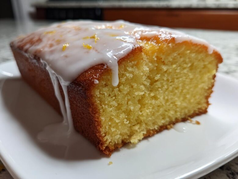 Close-up of a moist slice of lemon pound cake topped with thick white icing and lemon zest.