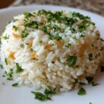 Close-up of a perfectly molded serving of fluffy rice pilaf topped with fresh chopped parsley and visible toasted pasta pieces.