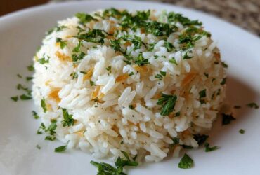 Close-up of a perfectly molded serving of fluffy rice pilaf topped with fresh chopped parsley and visible toasted pasta pieces.