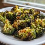 Close-up of perfectly roasted broccoli florets, slightly charred and sprinkled with Parmesan cheese, served on a white plate.