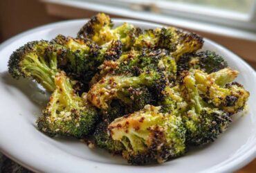 Close-up of perfectly roasted broccoli florets, slightly charred and sprinkled with Parmesan cheese, served on a white plate.