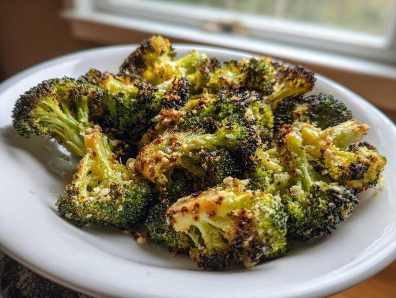 Close-up of perfectly roasted broccoli florets, slightly charred and sprinkled with Parmesan cheese, served on a white plate.