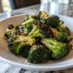 Close-up of crispy, charred roasted broccoli florets sprinkled with grated Parmesan cheese.
