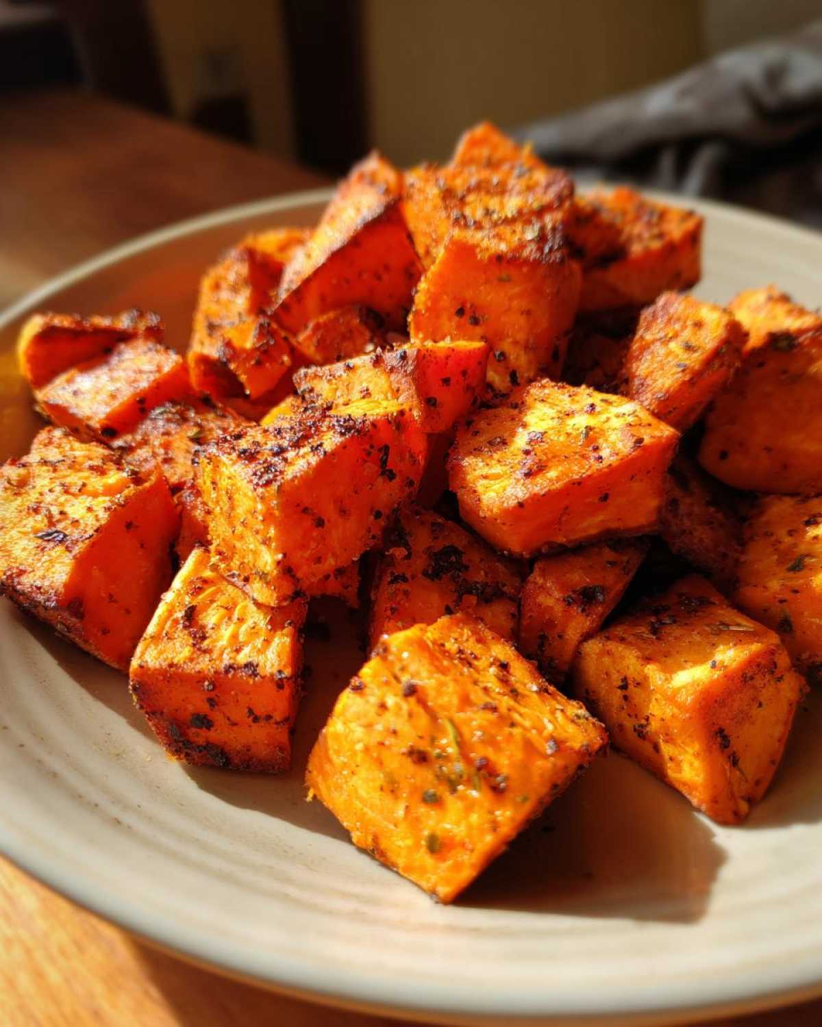 Close-up of perfectly seasoned and caramelized roasted sweet potato cubes piled on a light-colored plate.