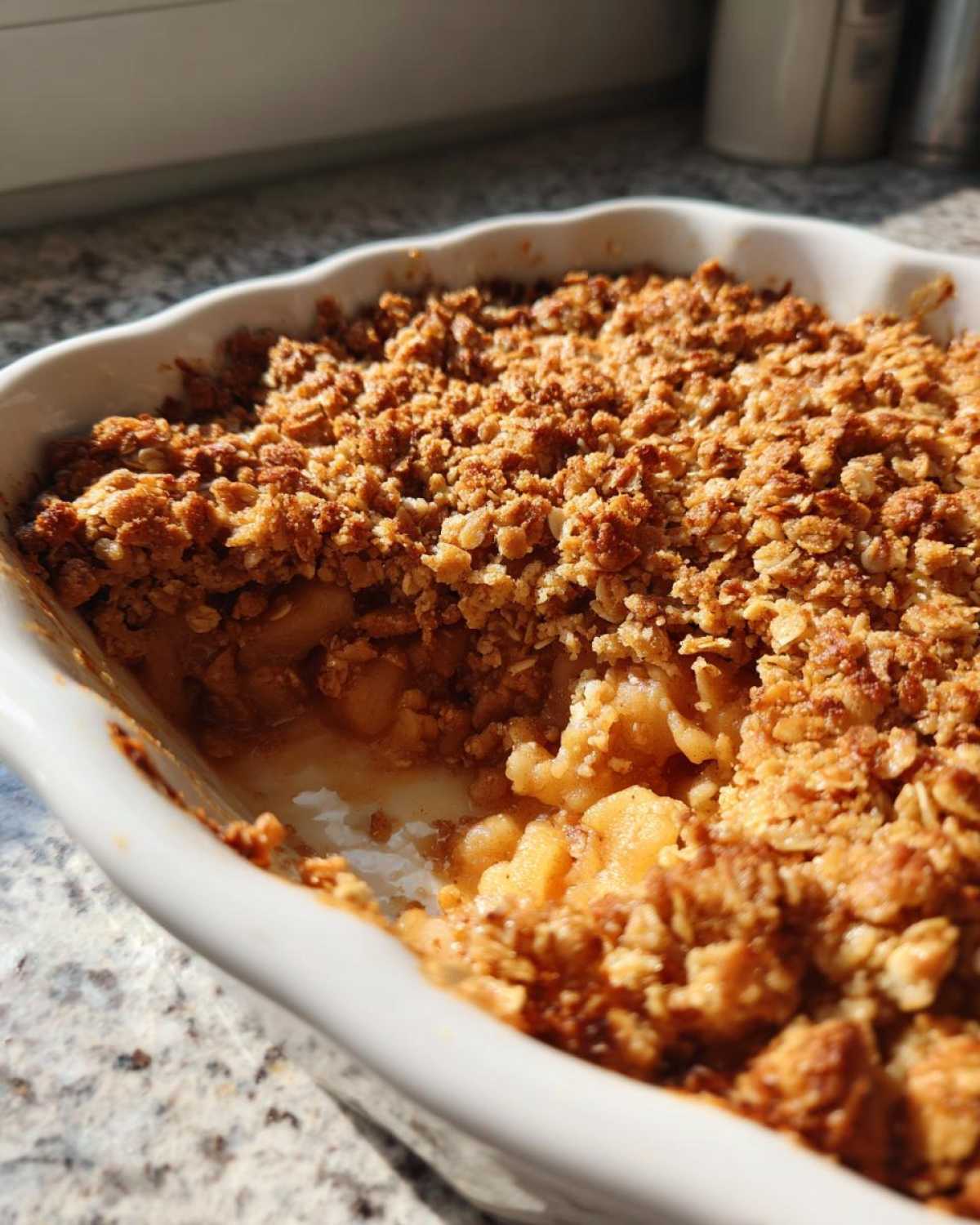 Close-up of a baked apple crisp recipe with a golden, crunchy oat topping and visible cooked apples inside a white baking dish.