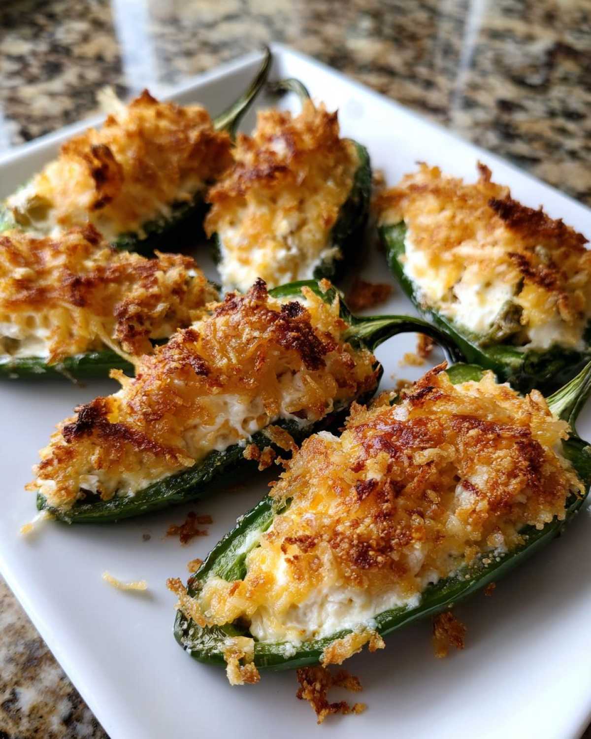 A plate of six baked Jalapeño poppers stuffed with cream cheese and topped with a golden, crispy breadcrumb crust.