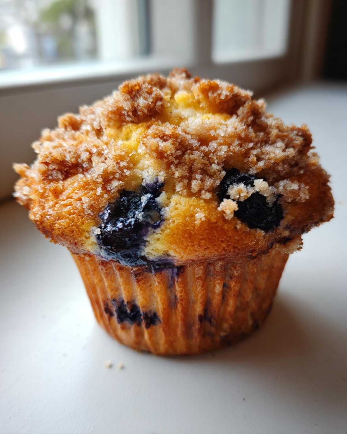 Close-up of a golden-brown blueberry muffin topped with a thick, sugary cinnamon streusel topping.