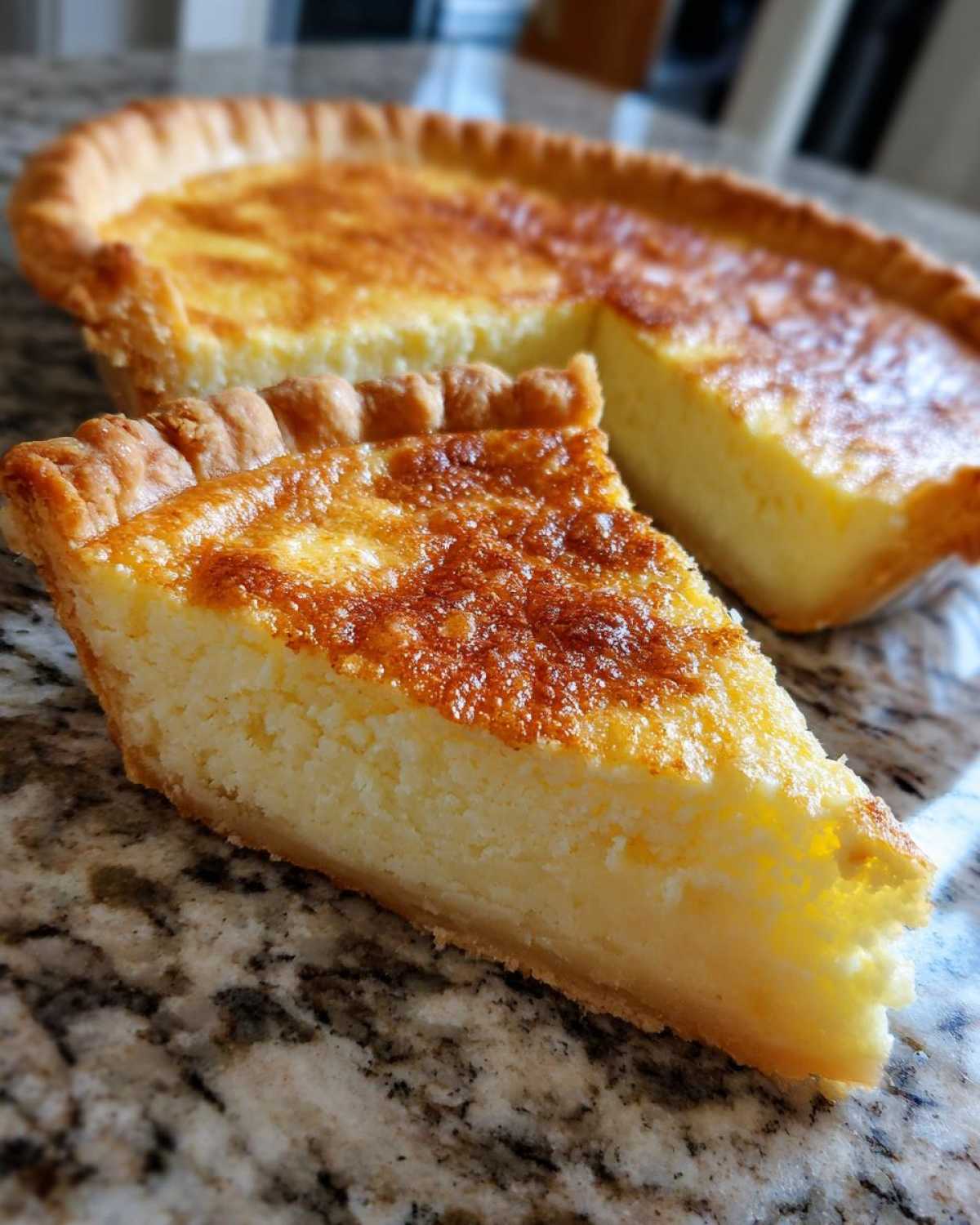 A close-up slice of creamy buttermilk pie with a beautifully browned top, sitting next to the rest of the pie.