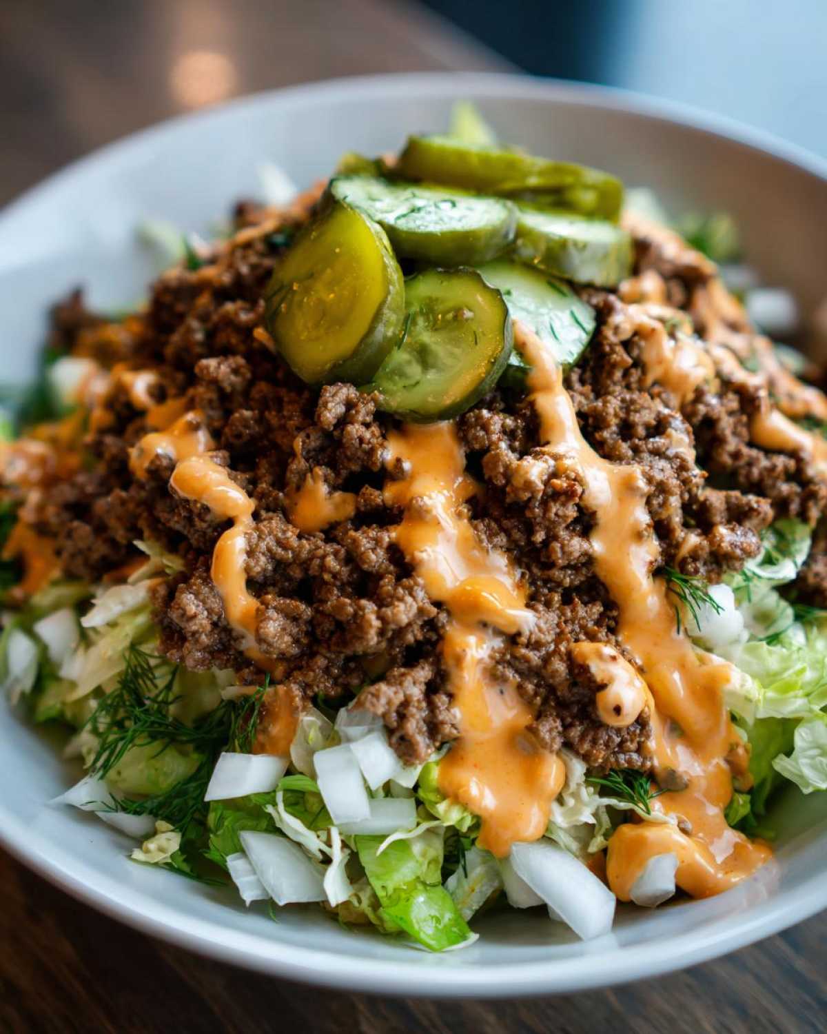 Close-up of a delicious cheeseburger bowl featuring seasoned ground beef, lettuce, onions, pickles, and a creamy orange sauce.