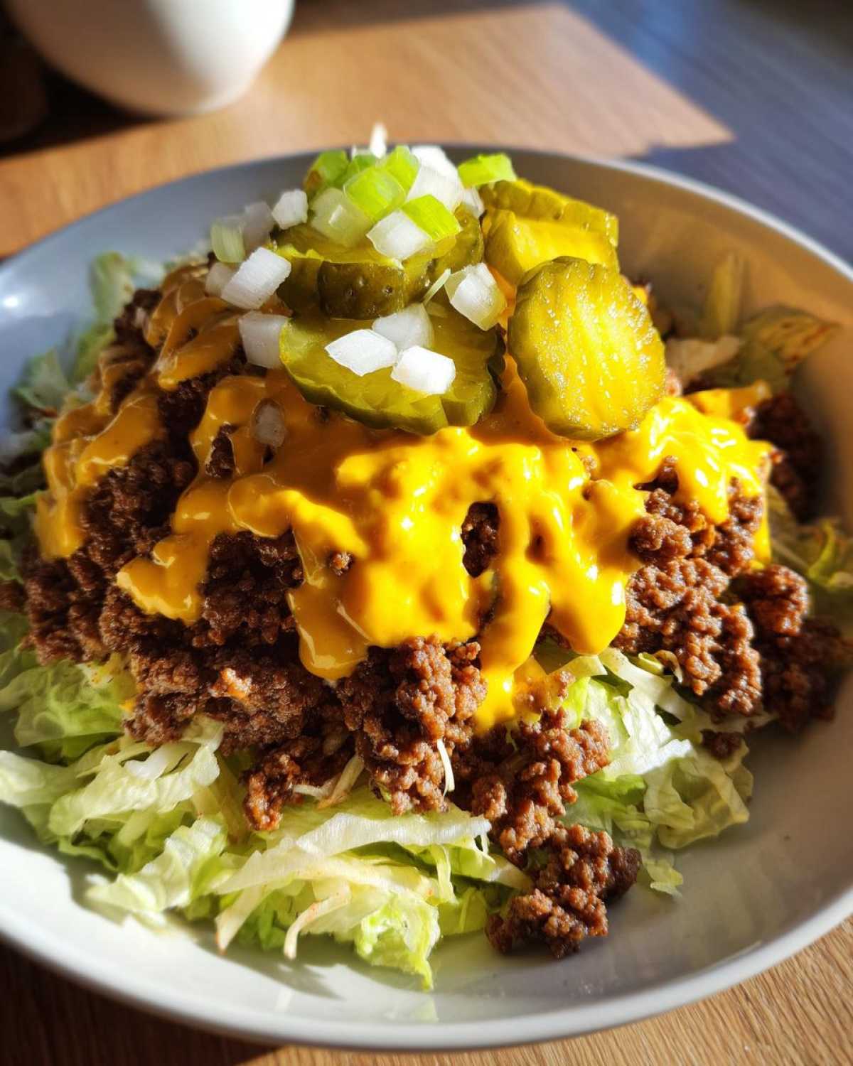 A close-up of a delicious cheeseburger bowl featuring ground beef, melted cheese sauce, pickles, and onions over shredded lettuce.