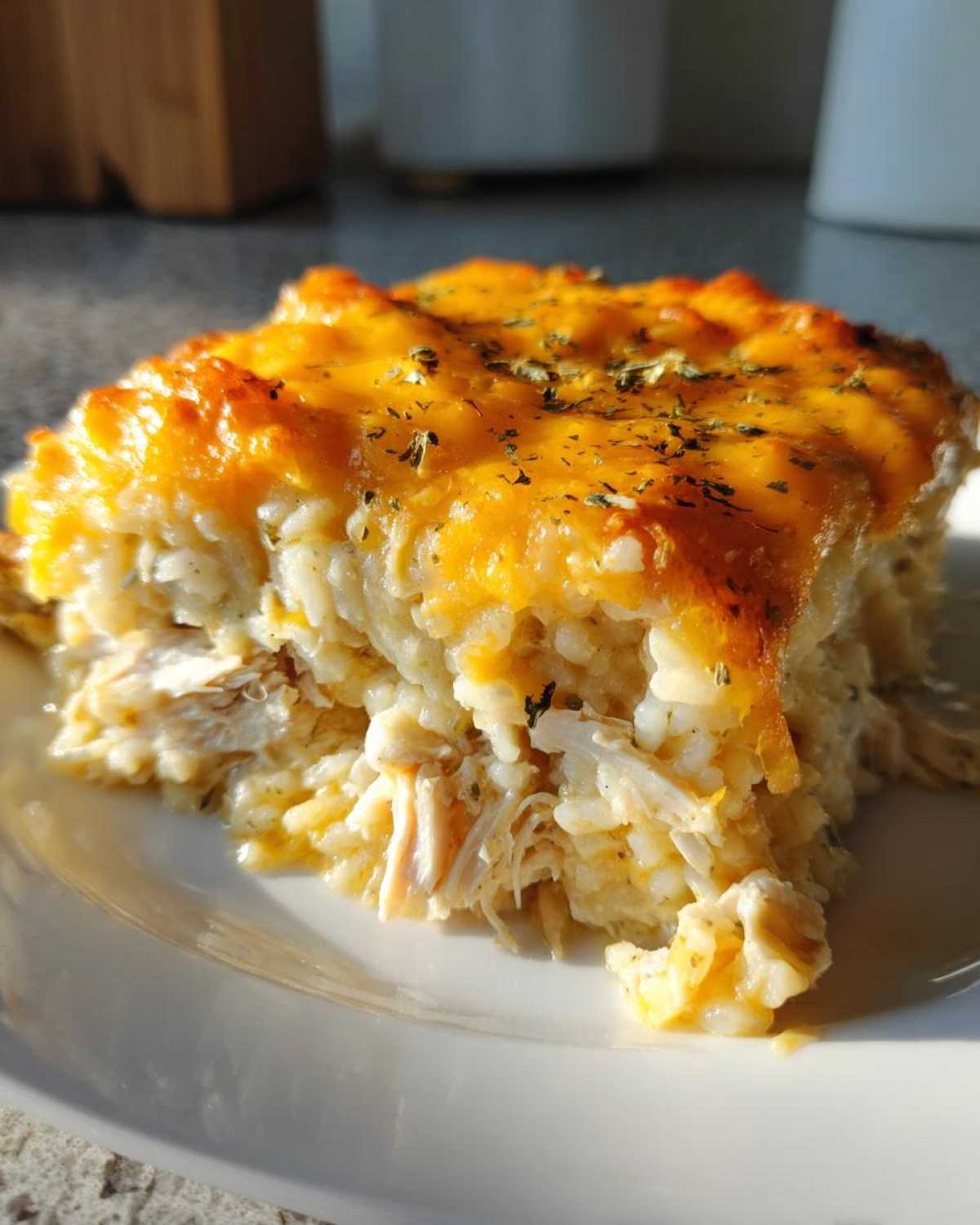 A close-up serving of cheesy chicken and rice, topped with melted cheddar and herbs.