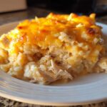 A close-up of a scoop of creamy, baked cheesy chicken and rice casserole topped with melted cheddar cheese.