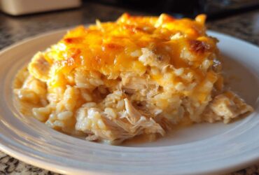 A close-up of a scoop of creamy, baked cheesy chicken and rice casserole topped with melted cheddar cheese.