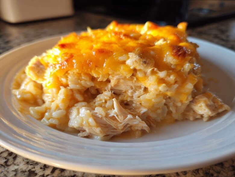 A close-up of a scoop of creamy, baked cheesy chicken and rice casserole topped with melted cheddar cheese.