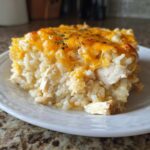 A square serving of cheesy chicken and rice casserole topped with melted cheddar cheese and herbs.