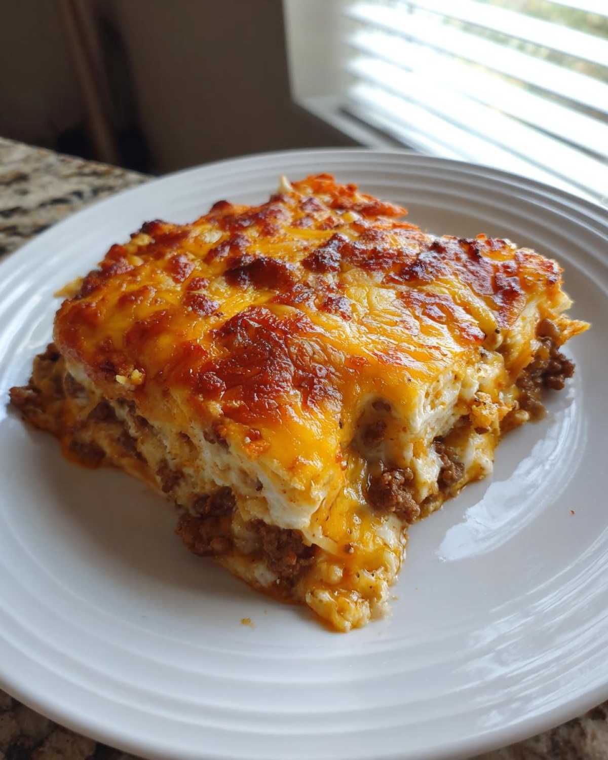 A square serving of Dorito Casserole topped with bubbly, melted cheddar cheese, showing layers of meat filling.