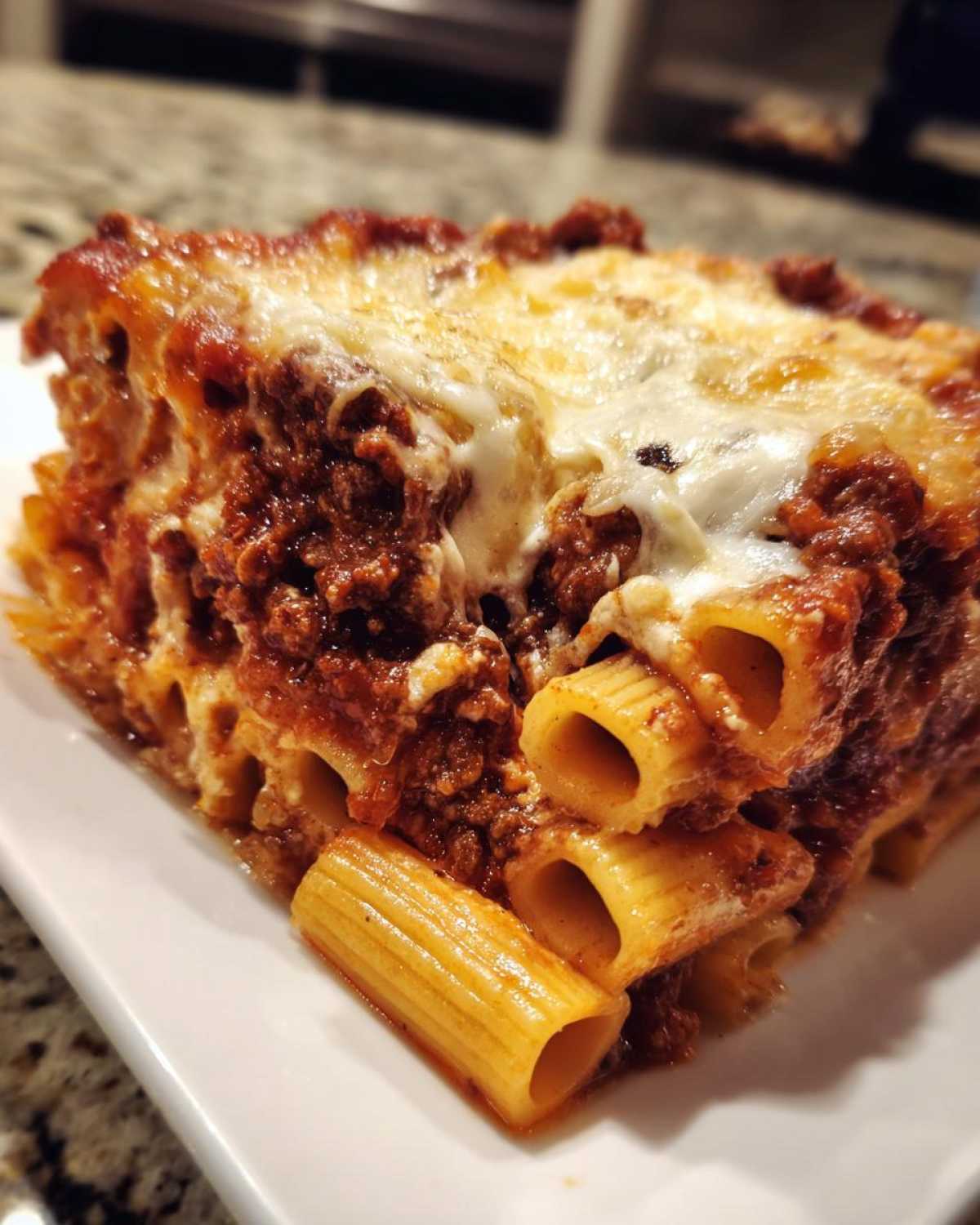 Close-up of a hearty slice of cheesy pasta bake with rigatoni noodles and rich meat sauce.