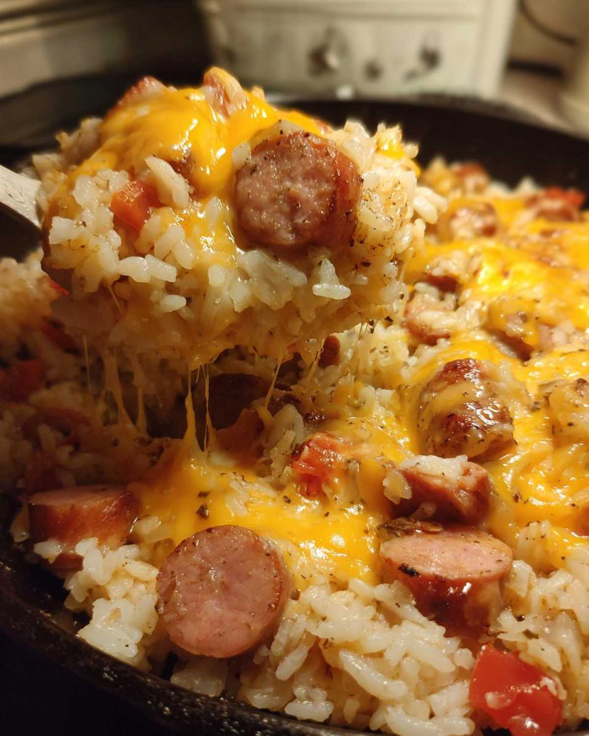 A wooden spoon lifting a scoop of cheesy sausage and rice, showing melted cheese strings.