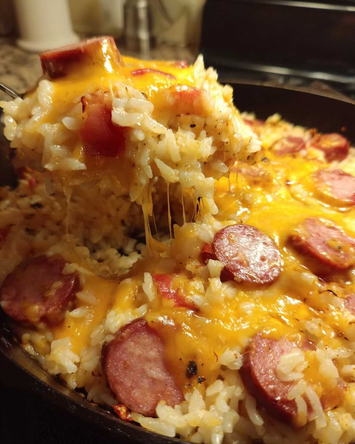 Close-up of cheesy sausage and rice being lifted from a skillet, showing melted cheese strings.