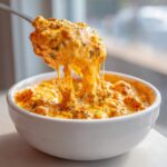A spoonful of hot, cheesy rotel dip showing long cheese pulls over a white bowl.