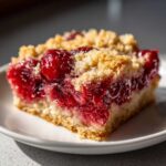Close-up of a square slice of moist cherry dump cake with a thick, bright red cherry filling and a crumbly topping.