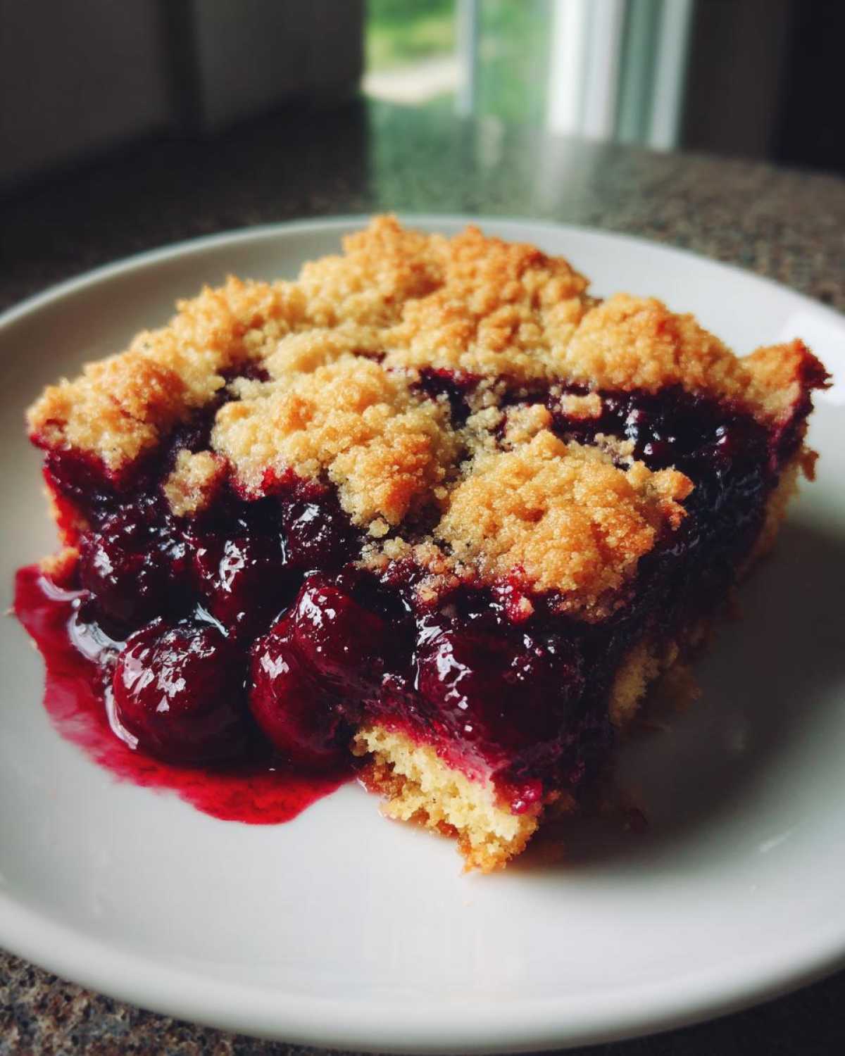 A close-up of a moist slice of cherry dump cake with a crumbly topping on a white plate.