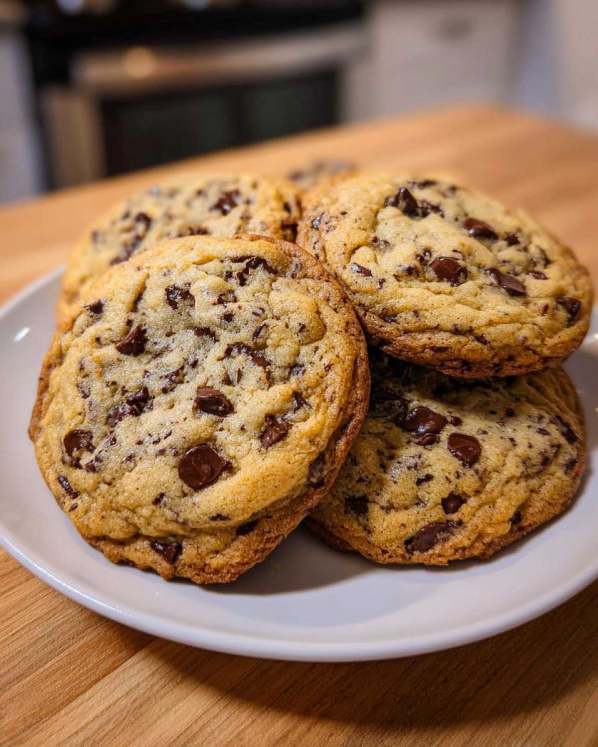 A close-up shot of several golden brown chewy chocolate chip cookies stacked on a white plate.