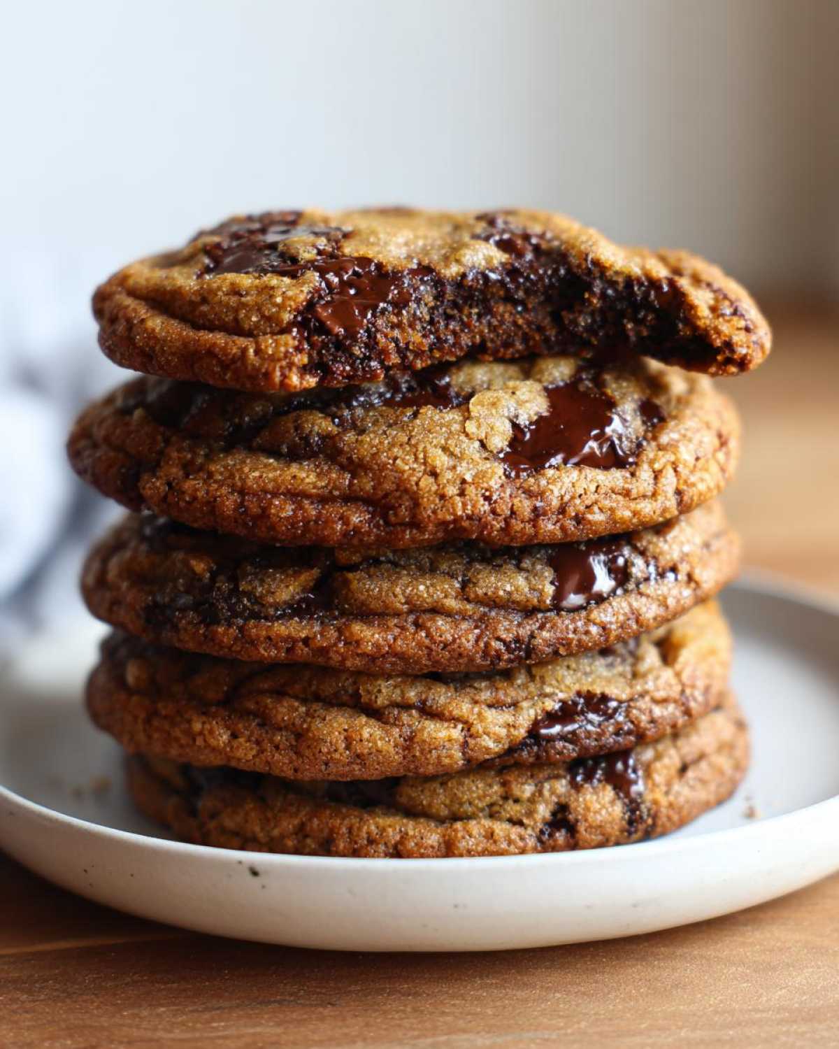 A tall stack of five perfectly baked, chewy chocolate chip cookies with gooey melted chocolate oozing out.