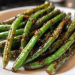 Bright green, glossy Chinese green beans with garlic sauce piled on a white plate.