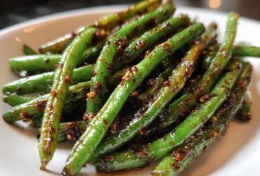 Bright green, glossy Chinese green beans with garlic sauce piled on a white plate.