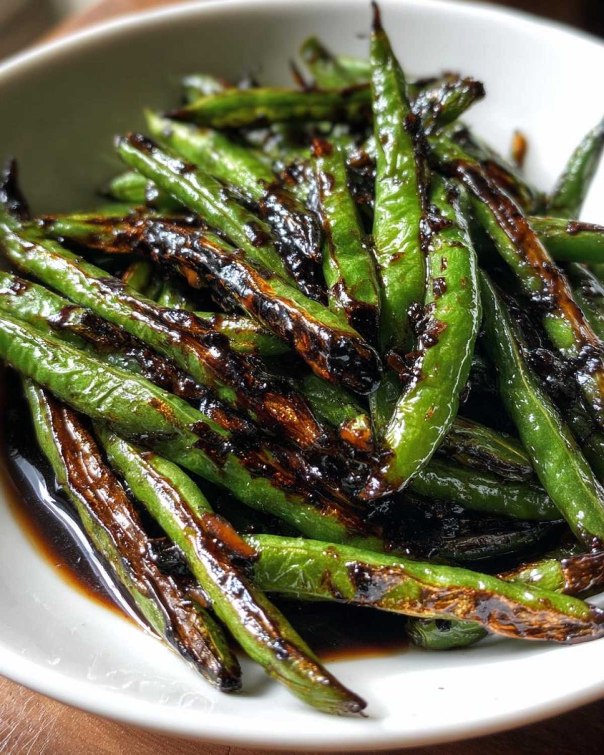 Close-up of blistered, vibrant green chinese green beans with garlic sauce in a white bowl.