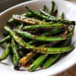 Close-up of vibrant green beans coated in a savory, dark garlic sauce, ready to eat.