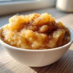 A close-up of chunky, homemade applesauce topped with cinnamon in a white bowl.