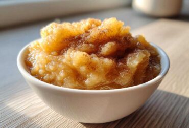 A close-up of chunky, homemade applesauce topped with cinnamon in a white bowl.