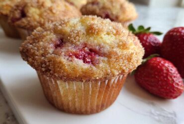 A close-up of a freshly baked strawberry muffin topped with cinnamon sugar, next to whole fresh strawberries.