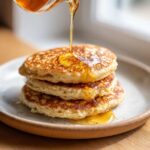 A stack of three fluffy coconut flour pancakes being drizzled generously with golden syrup.