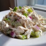 A mound of creamy cottage cheese chicken salad mixed with chopped celery and red onion served on a white plate.