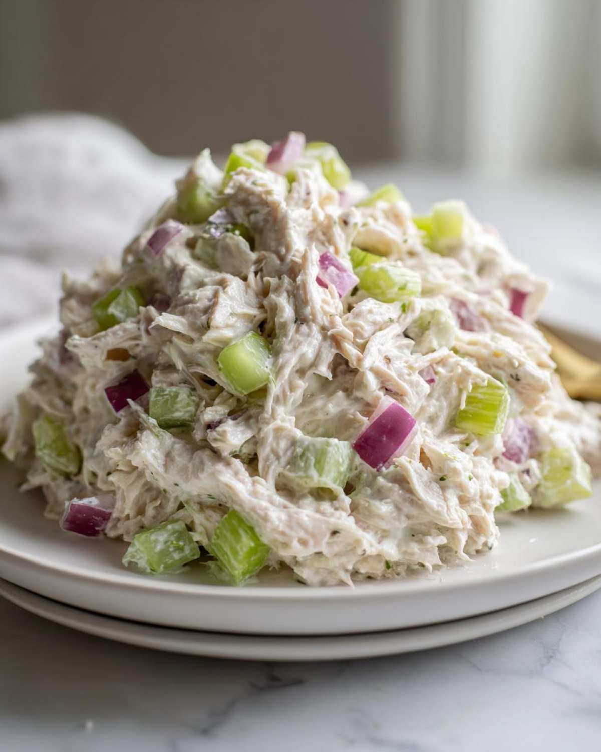 A mound of creamy cottage cheese chicken salad mixed with diced celery and red onion served on a white plate.