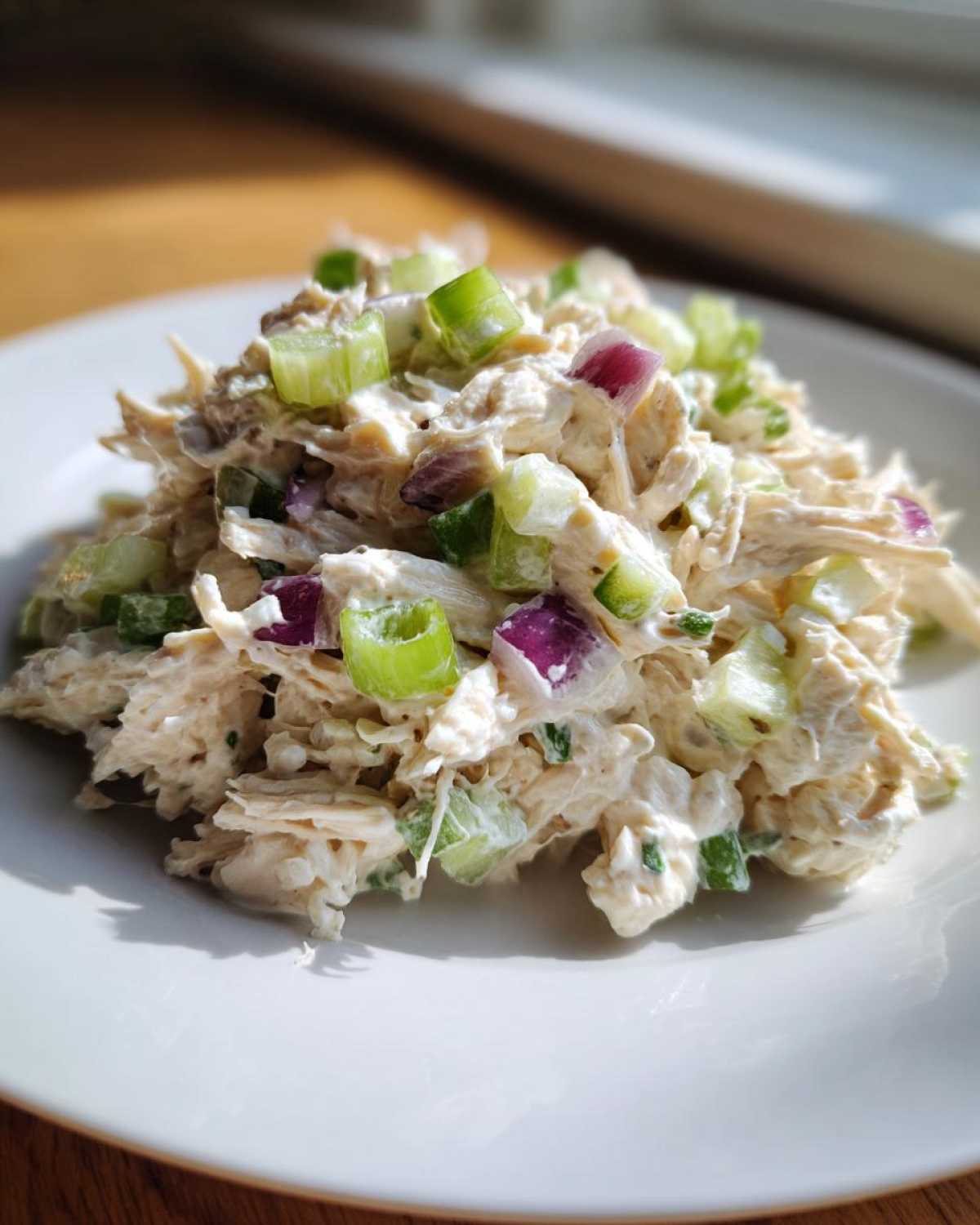 Close-up of a mound of creamy cottage cheese chicken salad topped with diced celery and red onion.