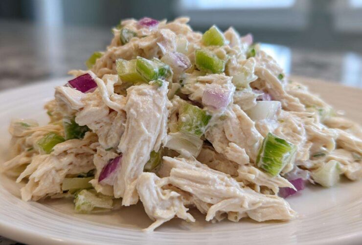 Close-up of a mound of creamy cottage cheese chicken salad mixed with chunks of celery and red onion on a white plate.