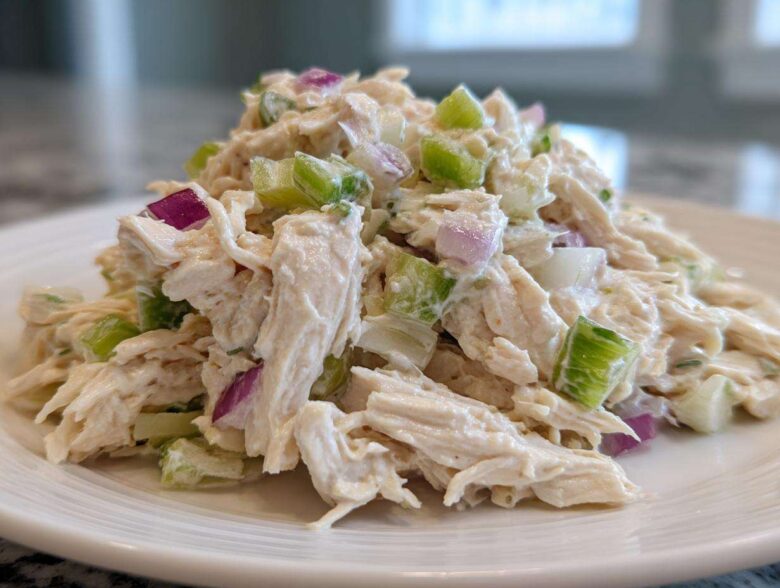 Close-up of a mound of creamy cottage cheese chicken salad mixed with chunks of celery and red onion on a white plate.