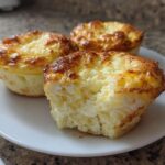 Three golden-brown cottage cheese egg cups starbucks hack style on a white plate, one is bitten into.