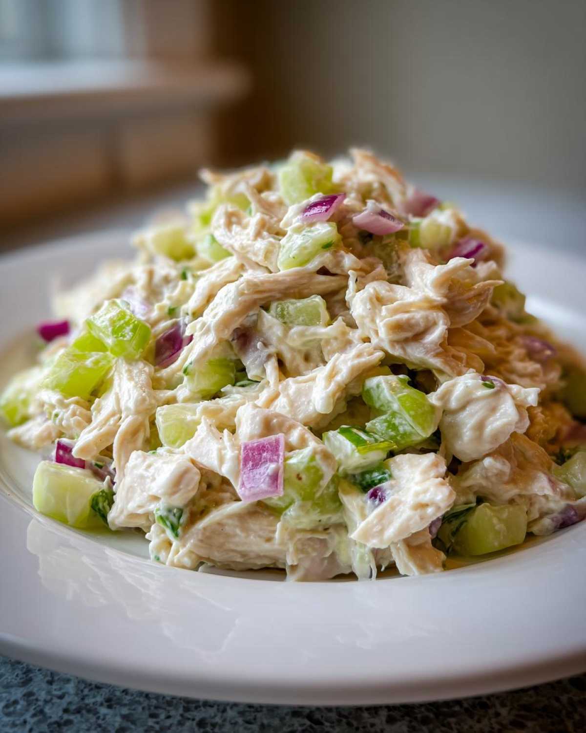 A mound of creamy cottage cheese chicken salad mixed with celery and red onion served on a white plate.