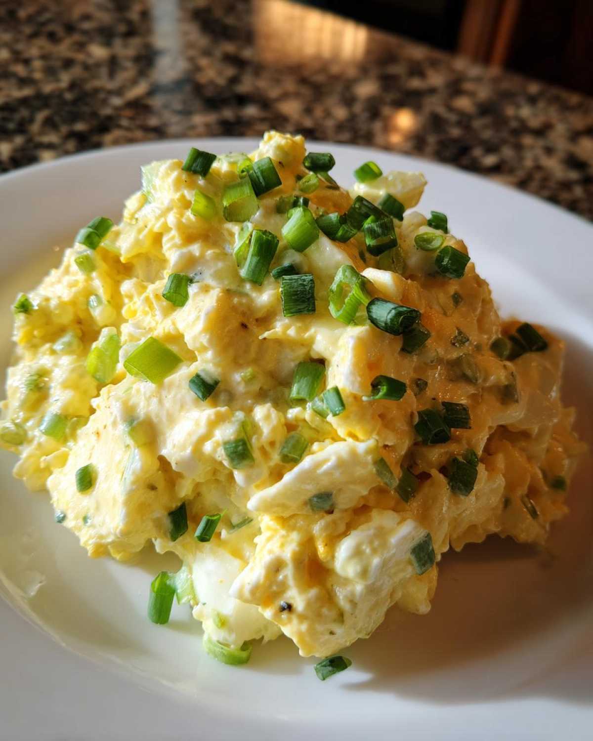 A mound of creamy egg salad recipe generously topped with freshly chopped green onions or chives on a white plate.