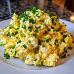 A generous mound of creamy egg salad recipe garnished heavily with freshly chopped green chives on a white plate.