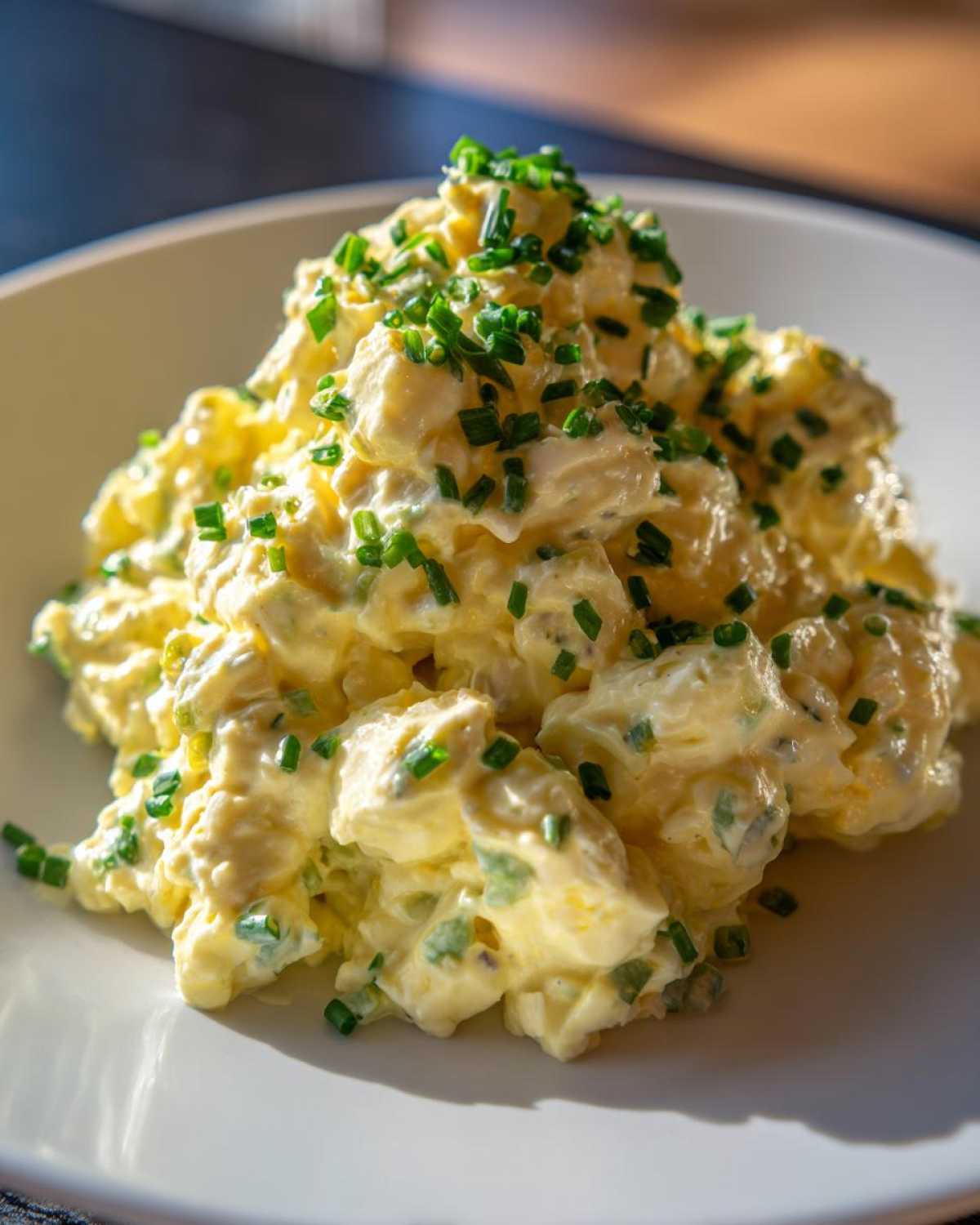Close-up of creamy egg salad recipe piled high on a white plate and garnished generously with chopped green chives.
