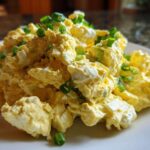 Close-up of a mound of creamy egg salad recipe garnished generously with chopped green onions on a white plate.